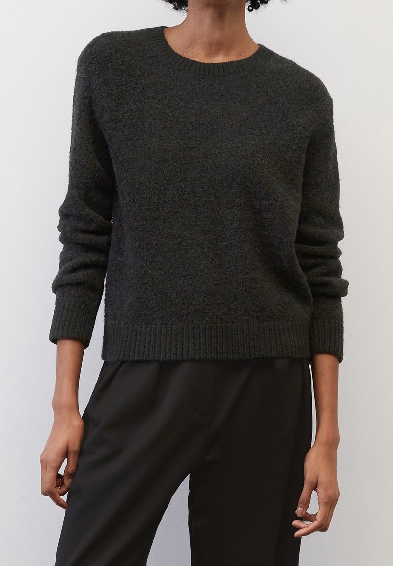 Pull en laine gris foncé avec un col rond, des poignets et un ourlet côtelés, doté d'une texture douce et d'une coupe décontractée, assorti à un pantalon noir.
