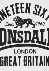 Fehér pamut póló, merész fekete felirattal és oroszlán grafikával. A felirat tartalmazza: "Lonsdale," "London," "Great Britain," és "Since 1960."