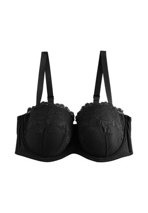 Bretelle de soutien-gorge en dentelle noire avec broderie florale portée sur l'épaule et le haut de la poitrine d'une personne à teint moyen.