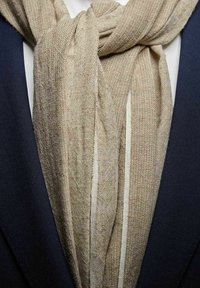 Beige, struktureret tørklæde hængende løst, med lyse vertikale striber, parret med en mørk skræddersyet jakke. Stoffet virker let og vævet.