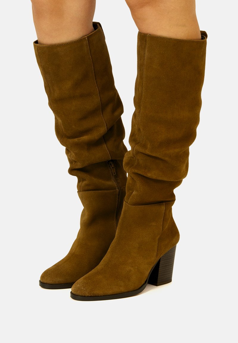 Stivali alti in suede marrone con design morbido, punta quadrata e tacco spesso nero. Dettaglio con zip laterale per una facile calzata.