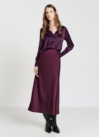 Blusa in seta a maniche lunghe e gonna lunga abbinata di un profondo viola. L'outfit presenta una chiusura con bottoni sul davanti e un tessuto liscio e fluttuante.
