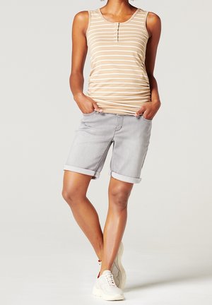 Vaaleanruskea raidallinen trikootoppi pyöreällä pääntiellä ja napituksella, yhdistetty harmaisiin farkkushortseihin, joissa on käännetyt reunat. Päällä vaaleat tennarit.