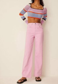 Virkat kort topp med flerfärgade ränder, tillsammans med hög midja, vida rosa jeans i denim. Platta svarta sandaler fulländar looken.