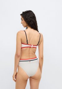 Σετ μπικίνι με ύφασμα σε ανοιχτό μπεζ χρώμα. Το πάνω μέρος διαθέτει ρυθμιζόμενους ιμάντες σε ναυτικό μπλε και κόκκινο, ενώ το κάτω μέρος έχει κόκκινη και ναυτικομπλέ ρίγα στη μέση.