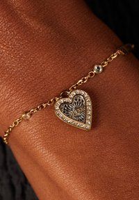 Gouden armband met een hartvormige bedel met een getextureerd middenstuk, omringd door heldere rhinestones. Ketting inclusief kleine ronde accenten.