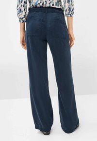 Pantalons larges navy avec une taille élastique, deux poches arrière et une texture lisse. Les poignets sont légèrement froncés pour plus de confort.