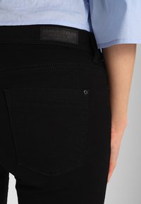 Jeans de mezclilla negros con un bolsillo trasero que presenta un remache plateado, complementados con una tela texturizada y una etiqueta de marca de cuero en la cintura.