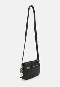 Sort læder crossbody-taske med justerbar rem, to rum med lynlås, guldfarvet hardware og en mærkevare-nøglering som pynt.