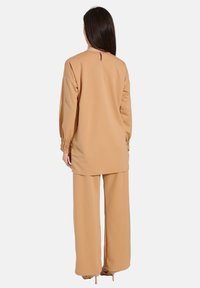 Lys beige to-delt sæt bestående af en lang tunika med elastiske manchetter og vide bukser. Glat stof med en let løs pasform.