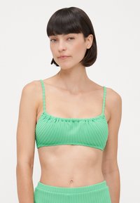 Top bikini verde a costine con spalline sottili, dettagli arricciati e finitura testurizzata. Tessuto morbido con un design senza cuciture.