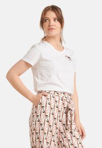 Witte t-shirt met korte mouwen en ronde halslijn, versierd met een eenvoudig, multicolor bladerenontwerp, gecombineerd met gestreepte, high-waisted broek.