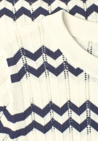 Pull en tricot blanc avec des rayures en zigzag bleu marine et des détails verticaux en tricot ajouré, avec un col rond côtelé.