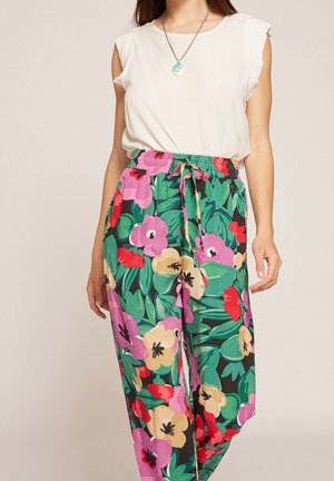 Mujer con un top blanco sin mangas y pantalones de talle alto con un estampado floral colorido y cintura con cordón.