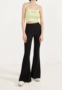 Ljusgrön ribbad crop top med spagettiband och svarta utsvängda byxor, som har hög midja och slät struktur. Vita sneakers på fötterna.