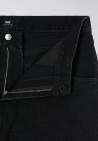 Pantaloni in denim nero con zip davanti e chiusura a bottone. Presentano una vita alta e un design a cinque tasche. La texture sembra resistente.