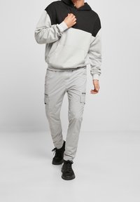 Pantalon cargo gris clair avec multiples poches, associé à un sweat à capuche bicolore noir et gris clair. Comprend une capuche à cordon de serrage.