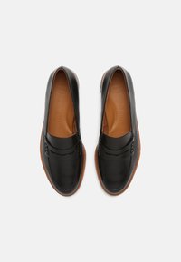 Mocasines de piel negra con un acabado suave, costuras detalladas, una banda en el antepié y una suela de goma marrón. Diseño ligero.