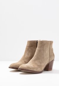 Brązowe zamszowe botki sięgające kostki z ostrym noskiem, niskim obcasem i dekoracyjnymi przeszyciami po bokach. Zamek błyskawiczny z tyłu.