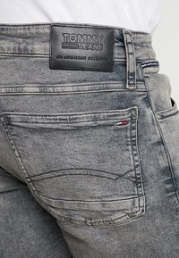 Jeans de mezclilla gris con una etiqueta de cuero de Tommy Jeans en la parte trasera de la cintura, costuras en contraste y un pequeño logo bordado en el bolsillo.
