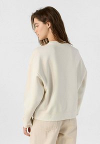 Felpa color crema con vestibilità comoda, colletto rotondo, spalle abbassate e superficie liscia, abbinata a pantaloni beige chiaro.