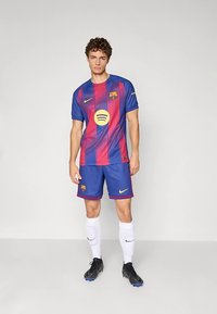 Camisola de futebol do FC Barcelona da Nike com riscas verticais vermelhas e azuis, calções combinando, logótipo amarelo da Spotify e chuteiras pretas com meias brancas.
