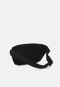 Sac bandoulière noir en tissu avec une surface en maille texturée, une sangle ajustable et une forme incurvée pour un design compact.