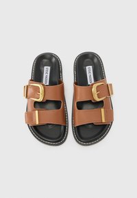 Sandales en plastique marron avec deux lanières, dotées de grandes boucles dorées et d'une semelle noire avec des détails en surpiqûre blanche.