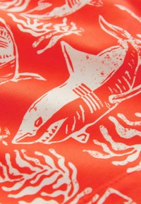 Tissu rouge présentant un motif de requin blanc avec des éléments et textures stylisés. Le design inclut des détails suggérant le mouvement et la profondeur.