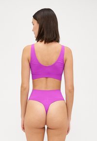 Vijolična športna modrček in visoko pasne bikini hlačke iz gladkega, raztegljivega materiala. Ima široke naramnice in minimalističen oblikovan hrbtni del.