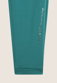 Culottes d'entraînement teal en tissu extensible. Présente un logo métallique "FREDDY" et un design ajusté et élégant avec des poignets élastiques en bas.