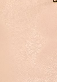 Perzikkleurig textuur leeroppervlak met fijne nerf en een kleine, gedeeltelijk zichtbare metalen sluiting in de rechterbovenhoek.