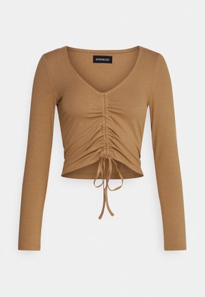 Ruskea, ribattu, pitkähihainen crop-top, jossa on V-kaula-aukko ja rypytetty etuosa. Alareunassa on nyöri, jonka avulla voidaan säätää istuvuutta.