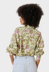 Blusa floreale realizzata in tessuto leggero, con un motivo colorato di fiori rosa e verdi, dalla vestibilità morbida e con maniche arrotolate.