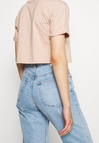 Lyhythihainen vaaleanpunainen t-paita, joka on leikattu lyhyeksi, yhdistetty vaaleansinisisiin korkeavyötäröisiin farkkuihin. Yksinkertainen muotoilu, pehmeä rakenne, näkyvät ompeluyksityiskohdat.