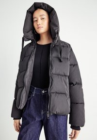 Black puffer jacket with a hood, featuring a zip closure, quilted texture, and elastic cuffs, paired with dark denim jeans.