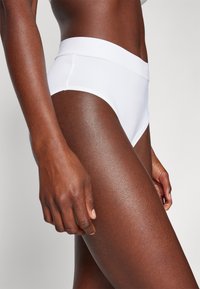 White cotton high-waisted briefs with a smooth texture. Features a wide elastic waistband, fitted design, and no visible patterns.