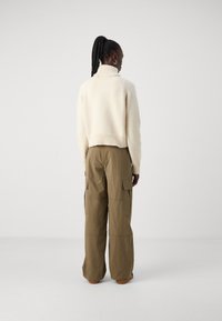 Hvid strikket sweater med høj krave, parret med løse cargos i olivengrøn. Materialet ser struktureret ud med tydelige syninger.