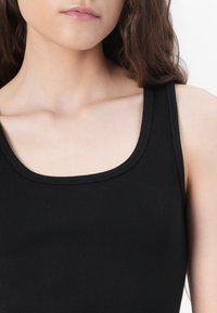 Black ribbed tank top featuring a wide, rounded neckline and thin shoulder straps. The ribbing adds texture and structure to the fabric.
