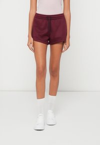 Μπορντό σόρτς φόρμας με ελαστική μέση και κορδόνι, με άνετη εφαρμογή και απαλό υφή. Συνδυάζονται με λευκές κάλτσες μέχρι τον αστράγαλο και αθλητικά παπούτσια.