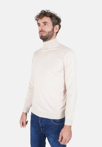 Maglione a collo alto color beige chiaro con design aderente, realizzato in materiale morbido. Presenta maniche lunghe e polsini e orlo a costine.