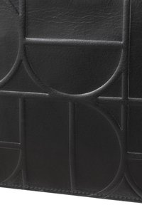 La pelle nera testurizzata presenta un motivo circolare impresso con linee incrociate, creando un design geometrico con una finitura opaca.
