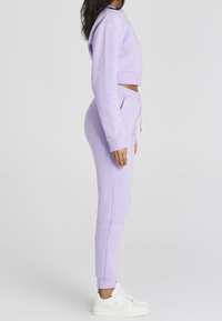 Světle fialová krátká mikina a matching tepláky z měkké látky, s šňůrkou v pase a žebrovanými manžetami. Nositá s bílými teniskami.