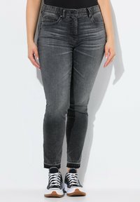 Jeans skinny de denim gris con una cintura de media altura, diseño de cinco bolsillos y dobladillo deshilachado. Combinados con zapatillas negras y blancas con suela de goma.