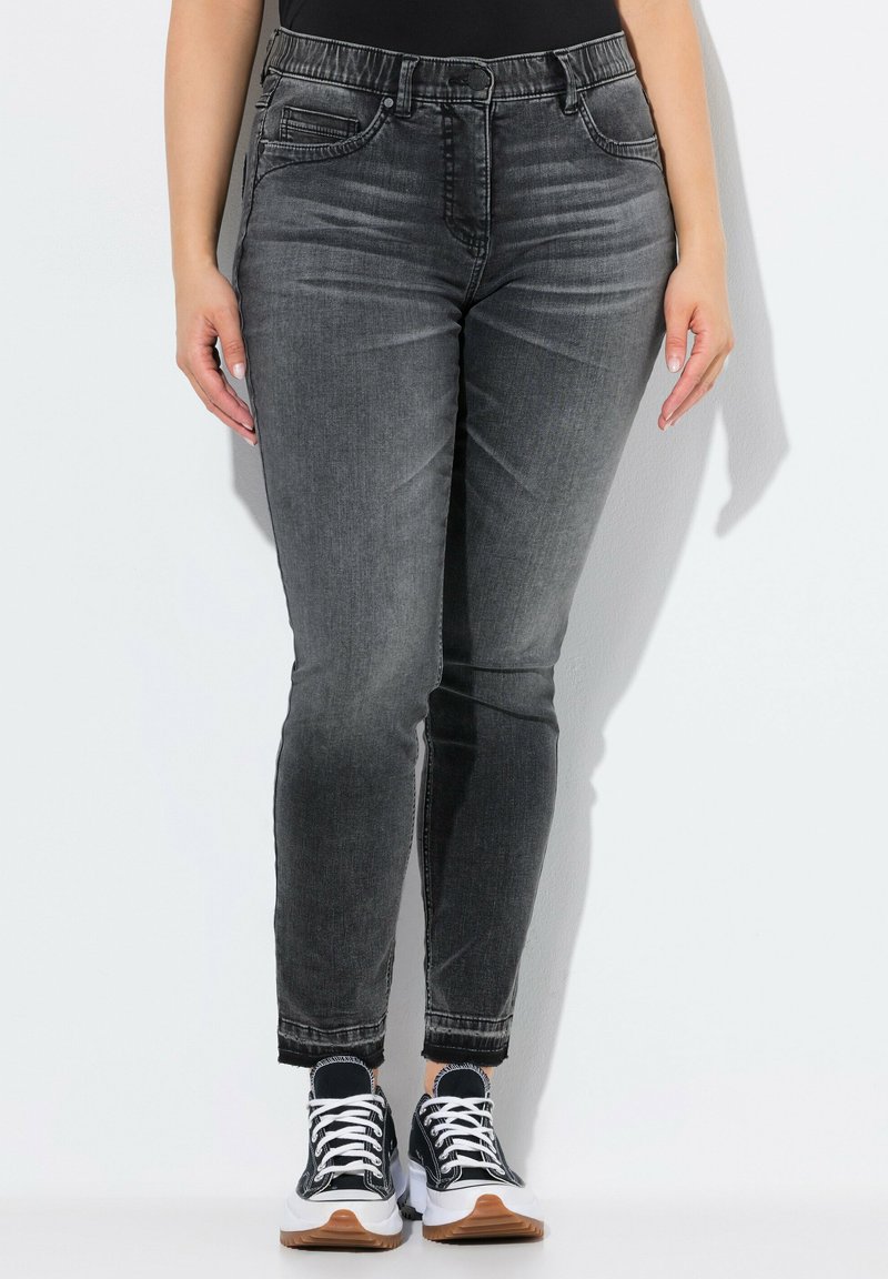Jeans skinny de denim gris con una cintura de media altura, diseño de cinco bolsillos y dobladillo deshilachado. Combinados con zapatillas negras y blancas con suela de goma.