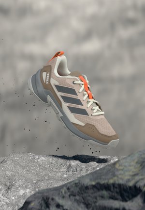 Beiger und grauer leichter Sportschuh mit Mesh-Obermaterial, orangen Akzenten und strukturierter Sohle, entworfen für Outdoor-Aktivitäten.