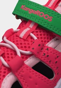 Εγγύς πλάνο ενός ροζ και λευκού αθλητικού παπουτσιού με αναπνεύσιμο δίχτυ, κόκκινες λουρίδες με μαύρες κηλίδες, λευκά ελαστικά κορδόνια και πράσινη λουρίδα με την επιγραφή "KangaROOS".