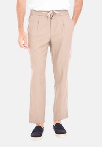 Pantaloni beige a pieghe realizzati in tessuto leggero, dotati di vita con cordino e tasche laterali. Abbinati a espadrillas blu navy.