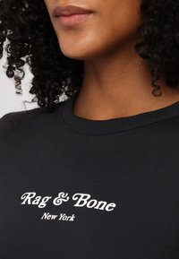 Gros plan d'une personne portant un t-shirt noir à col rond avec un texte blanc « Rag & Bone New York » sur la poitrine.