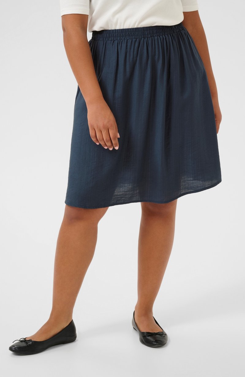 Navy blue, knee-length skirt made of lightweight fabric with an elastic waistband. Worn with black flat shoes featuring a bow detail.